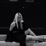 Elegant black and white portrait of a woman in urban fashion sitting on steps.